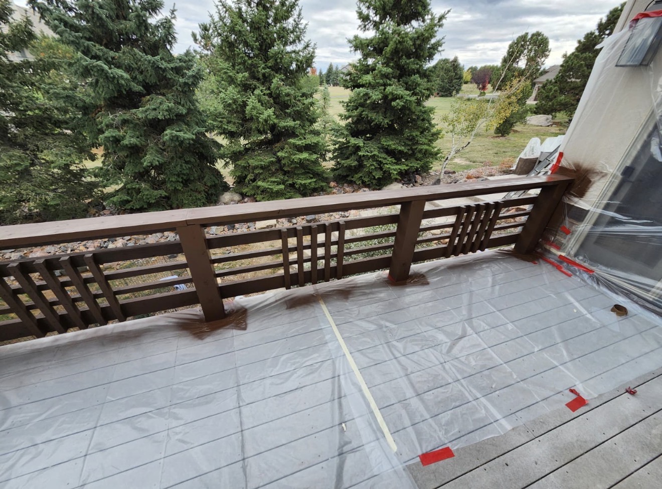 Deck boards being stained with the railings masked and protected